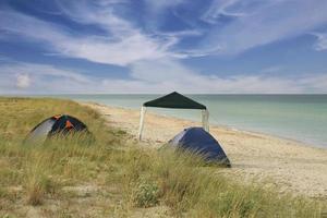 camping y tienda turística en una costa salvaje junto al mar, temprano en la mañana contra un cielo azul con nubes. foto