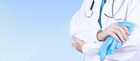 Healthcare and medical concept. A doctor with a stethoscope in his hand, in a white coat and blue gloves with crossed arms. Side view. Copy space. photo