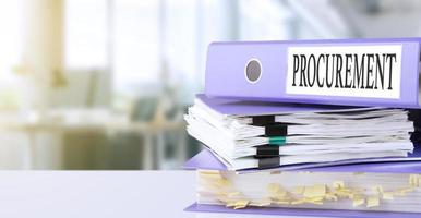 Procurement, text written in a folder with documents in trendy purple color, lying on a stack of papers, documents on an office table, against a background of soft blur office background. photo