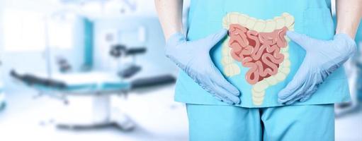 primer plano de una doctora cirujana con uniforme médico y un ícono del intestino con un intestino grueso en el fondo de la mesa de operaciones en el hospital, fondo suave y borroso. foto