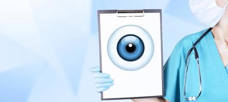 Realistic human eye with a blue cornea in the form of a round icon on a tablet in the hands of a doctor, a woman in medical clothes. Gradient blue background. Copy space. photo