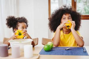 pequeña y linda hermana menor que se preguntaba e imitaba a su hermana mayor tratando de comer pimiento foto