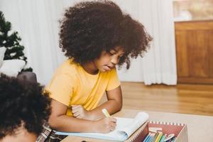 los niños negros americanos de la hija del preescolar hacen los deberes aprendiendo educación con su hermana viviendo juntos en casa. foto