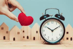 corazón de amor con reloj de tiempo con fondo de casa de madera para tiempos para quedarse en casa concepto. foto
