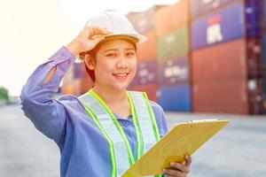 Portrait of Asian girl teen worker working in shipping cargo port import export working area with container box background. photo
