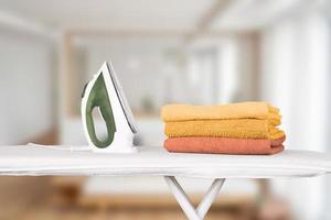 An electric iron stands on an ironing board and folded orange-colored bath towels, against the backdrop of a home interior. Blurred background, soft focus. photo