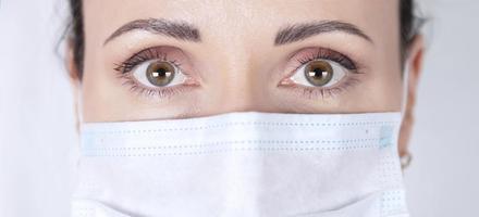 Piercing female look of brown eyes close-up. Portrait of a female doctor in a medical mask. photo