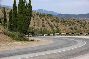 un giro brusco en el camino con una valla, en las altas montañas europeas y árboles de cipreses verdes y en crecimiento. foto