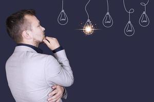 A businessman in a gray business suit, pensively looks at an electric light bulb, as an idea, business, development, startup. Side view. Copy space photo