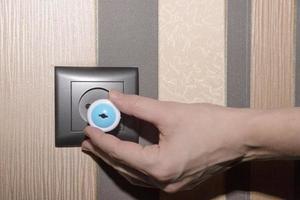 Brown electrical outlet on a brown tone wall and a woman's hand inserting a plug, child proof. photo