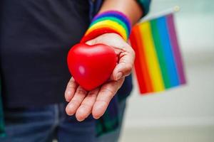 mujer asiática sosteniendo hert rojo con bandera del arco iris, derechos de símbolo lgbt e igualdad de género, mes del orgullo lgbt en junio. foto