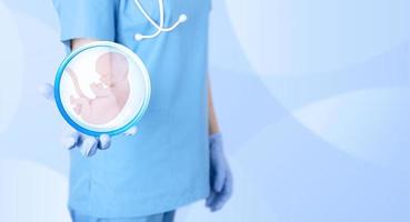 Embryo icon in the hands of a gynecologist doctor as a symbol of conception and in vitro fertilization. Blue medical background. Poster. photo