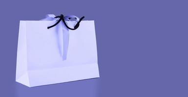 Blank shopping packaging mockup, white paper bag mockup with handles and bow on purple background Very Peri. Holiday gift. copy space. photo