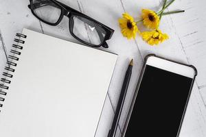 Note book with smartphone, reading glasses, pen and sunflowers on wooden desk. photo