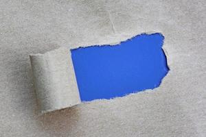 Text on torn hole in the sheet of brown paper on blue background. Copy space.