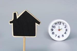 Wooden house model with blurred white alarm clock background. photo