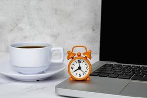 despertador en la computadora portátil con una taza de café en una mesa. el reloj puesto a las 8 en punto. foto