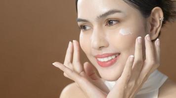 una mujer joven con una cara hermosa está sosteniendo crema, usando crema de su cara, concepto de belleza para el cuidado de la piel foto