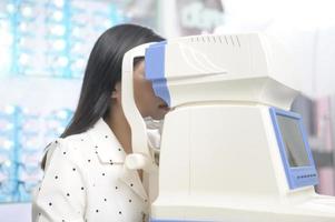 una joven clienta que está siendo examinada con una prueba visual usando un autorrefractor por un oftalmólogo en un centro óptico, concepto de cuidado de los ojos. foto
