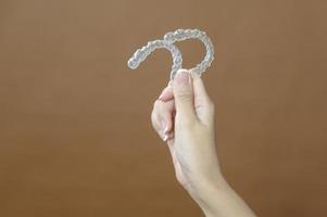 Close up young woman hand is holding Invisalign over brown background photo