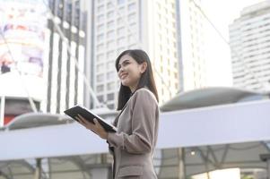 una joven y hermosa mujer de negocios está usando una tableta en una ciudad moderna, tecnología de negocios, concepto de estilo de vida de la ciudad foto