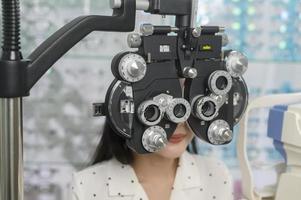 una joven clienta que está siendo examinada con una prueba visual usando un dispositivo de medición de la vista de optometría bifocal por un oftalmólogo en el centro óptico, concepto de cuidado de los ojos. foto