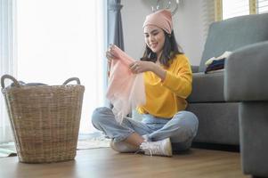 Young happy woman wearing yellow shirt folding clothes in living room, laundry concept photo