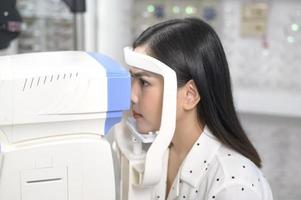 Young female customer being examined visual test using autorefractor by ophthalmologist in optical center, eyecare concept. photo