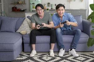 Young smiling gay couple playing video games in the living room at home, LGBTQ and diversity photo