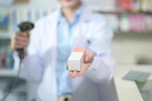 Farmacéutica femenina escaneando código de barras en una caja de medicamentos en una farmacia moderna. foto