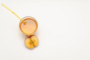 un vaso de jugo de manzana con una pajita y media manzana roja sobre un fondo blanco foto