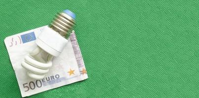 lámpara de bajo consumo y billete en euros sobre fondo verde, espacio de copia. foto