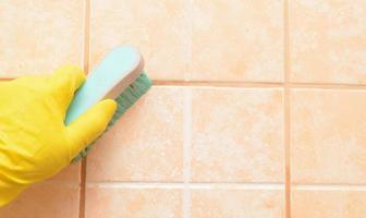 Limpieza de cerámica en el baño. cepillo en mano en guante económico amarillo, copyspace. protección de azulejos contra moho y hongos foto