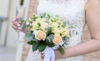 Bride holds wedding bouquet and empty champagne glass. photo