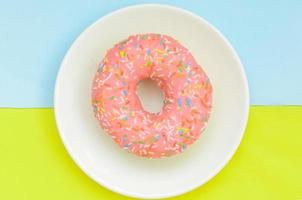 Top view, pink glazed donut on white plate on pastel green turquoise background.Sweet dessert for snack. photo