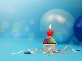 Sweet cupcake and bow candle on blue background with copy space. Happy birthday party photo