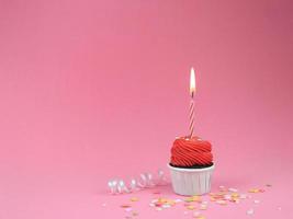 Sweet red cupcake with bow candle on pink background with copy space. Happy birthday party background concept. photo