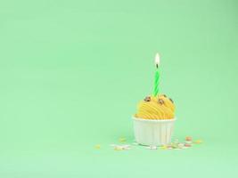 Sweet yellow cupcake with bow candle on green background with copy space. Happy birthday party background concept. photo