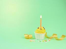 Sweet yellow cupcake with bow candle on green background with copy space. Happy birthday party background concept. photo