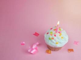 cupcake de feliz cumpleaños y vela de arco sobre fondo rosa con espacio de copia. foto