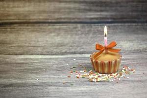 Happy birthday cupcake and bow candle on table on wooden background with copy space. Cute food happy birthday background concept photo