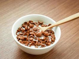 sabor a chocolate con cereales con cuchara y leche en un bol sobre una mesa de madera, desayuno listo para comer por la mañana foto