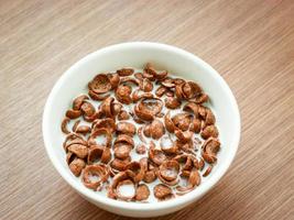 Cereal chocolate flavor with milk in whith bowl on wooden table, breakfast ready to eat in the morning photo