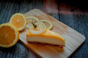 A piece of lemon cream cheese pie with fresh yellow lemon slices on wooden kitchen cutting board photo