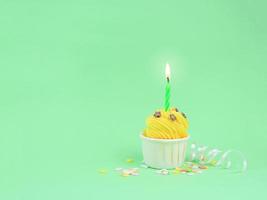 dulce cupcake amarillo con vela de arco sobre fondo verde con espacio para copiar. concepto de fondo de fiesta de feliz cumpleaños. foto