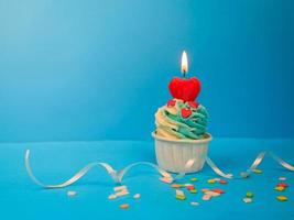 Sweet cupcake and bow candle on blue background with copy space. Happy birthday party photo