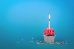 pastelito rojo dulce con vela de arco sobre fondo azul con espacio de copia. Fondo de concepto de fiesta de feliz cumpleaños.