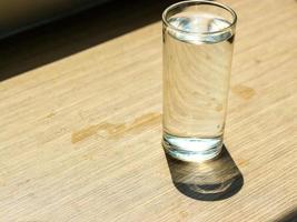 agua potable limpia en el vaso sobre una mesa de madera con el sol brillando a través de la ventana. foto