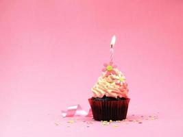 cupcake de feliz cumpleaños y vela de arco sobre fondo rosa con espacio de copia. foto