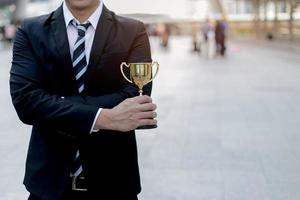 businessman, holding up a gold trophy cup is winner in a competition with city background. Win concept. photo